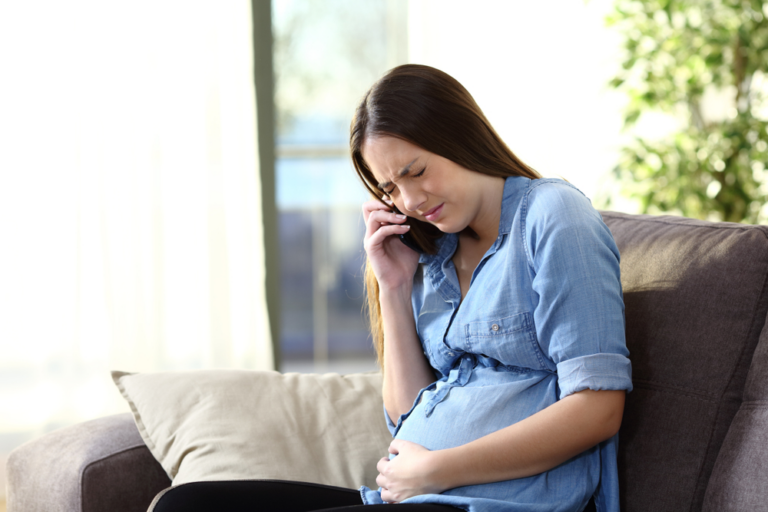 Pregnant woman in pain calling her doctor to prevent a birth injury