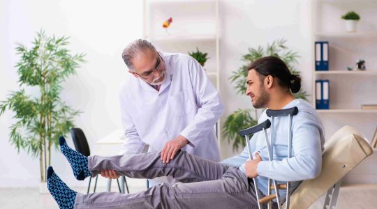 Young-leg-injured-man-visiting-old-doctor-osteopath